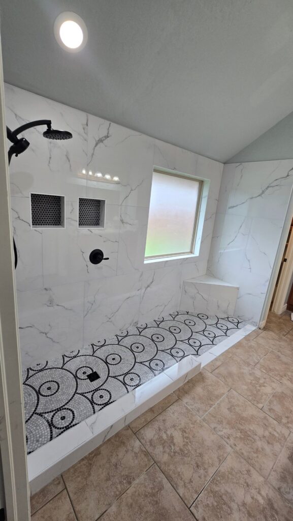 Large tiled shower with marble-look walls, a patterned mosaic floor, corner bench, two niches, and black fixtures in Oklahoma City.
