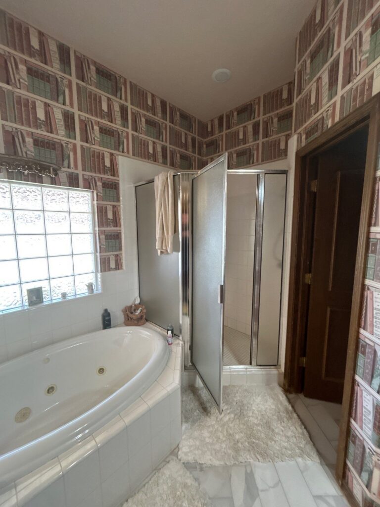 Older shower with a metal-framed glass enclosure beside a jetted bathtub before remodeling in Oklahoma City.