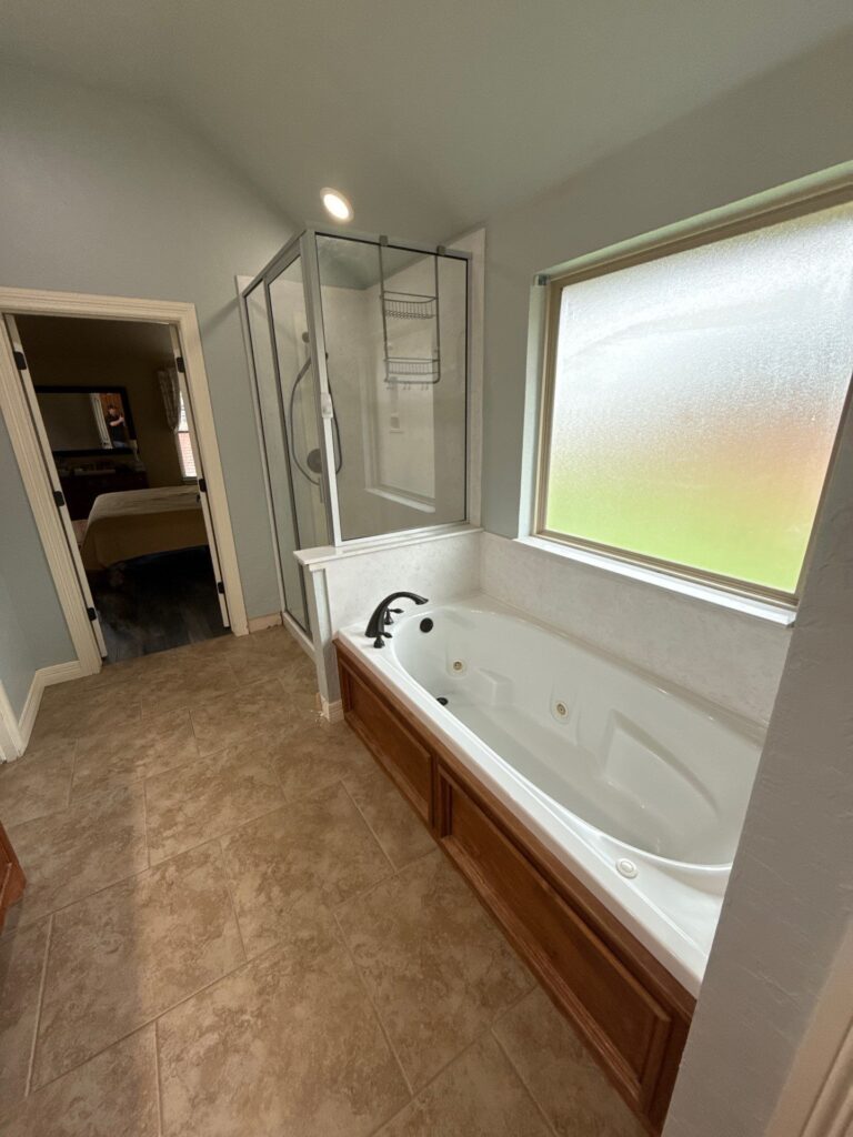 Jetted bathtub beneath a frosted window beside a separate framed shower before an Oklahoma City bath remodel.
